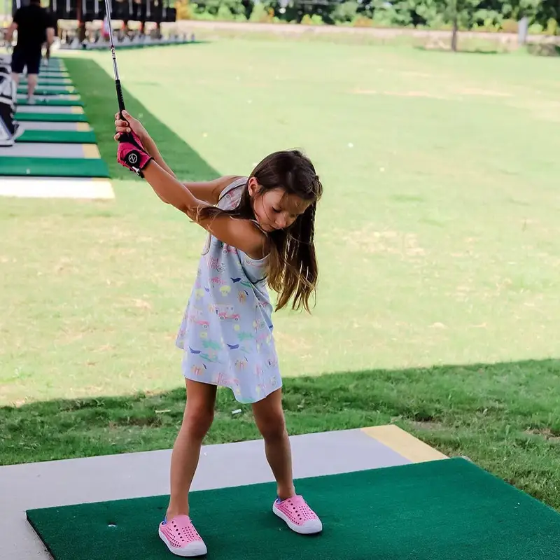 A young girl swings at Golfsuites's driving range.